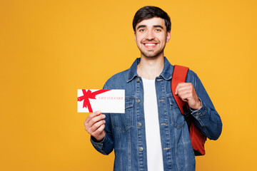 Young surprised boy student he wear denim casual clothes backpack bag hold gift certificate coupon voucher card for store isolated on plain yellow background. High school university college concept.