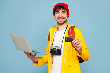 Traveler IT man wear yellow casual clothes hold laptop pc computer credit bank card isolated on plain blue background. Tourist travel abroad in free time rest getaway. Air flight trip journey concept.