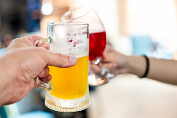 Close-up of two hands clinking beer and wine glasses in a blurred background, symbolizing celebration, social gathering, and friendship