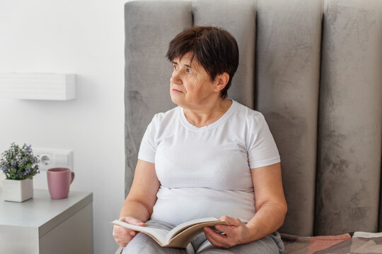 Senior woman reading book and looking thoughtful.