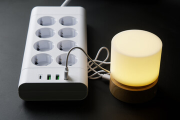A modern compact USB night light emitting a warm yellow glow, plugged into a multiport charging...