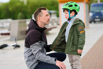 father instructing boy in green helmet on sidewalk next to scooter, emphasizing safety and bonding...