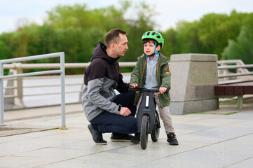 father teaching son balance bike fundamentals park setting, focused guidance bonding outdoor...
