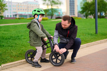 Fototapeta premium father teaching son balance bike riding in park. learning safety, outdoor activity, focus on bonding and guidance. urban background, fatherhood and child's development theme