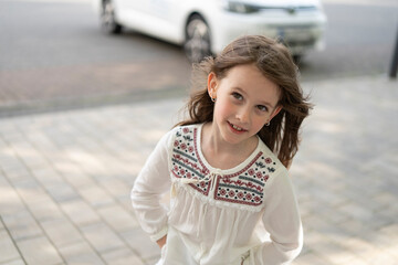 A smiling girl in a traditional Ukrainian embroidered shirt looks at the camera on the outdoors....