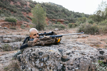 Hunter taking aim with rifle in natural landscape