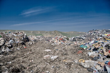 A garbage dump set against green hills and blue sky — a stark contrast between natural beauty and...