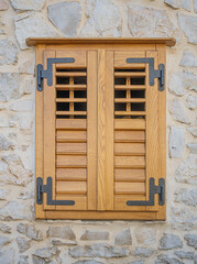 A traditional closed wooden shutter, featuring natural wood grain and sturdy black metal hinges, set against a rustic stone wall background, providing a charming architectural detail.