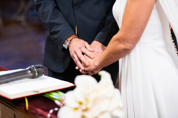 Una pareja casándose en una ceremonia religiosa, uniendo las manos, en el momento de la boda