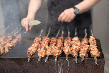 Men's hands spin kebab skewers on a charcoal grill in the smoke. Street food concept