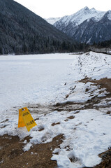 A frozen lake and field with snow-capped mountain landscape with caution sign yellow "CAUTION WET FLOOR" sign with English and Chinese Language. 