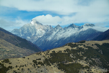Mount Siguniang (Four Sisters Mountain) in Sichuan, China. The prominent snow-covered peak, The foreground features brown hills contrasting with alpine backdrop and a wide, vivid blue sky 