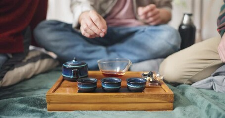 Close up a guy pours orange tea into Asian cups and holds a tea ceremony with his friends on a blanket at home