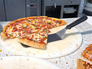 Freshly baked pizza with slice cut out on a white stone table. Melted cheese, meat, and crispy crust