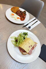 Two types of breakfast: traditional english with hash browns, bacon, mushrooms, tomato, fried eggs, Lincolnshire sausage, and continental with bread, sliced cold meats, cheese and salad.