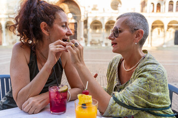 beautiful couple of middle-aged female friends enjoying an aperitif sitting at an outdoor coffee bar in a historic square