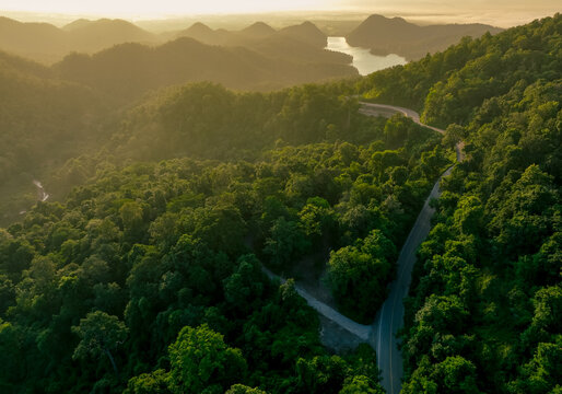 Fototapeta Landscape of green mountains with curve highway road and lake in the morning. Nature landscape. Watershed forest. Water and forest sustainability concept. Aerial view of mountain with green trees.