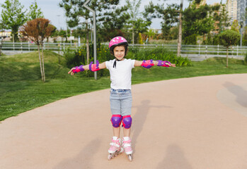 A little curly-haired girl rollerskates within the necessary facilities in the city. In a helmet...