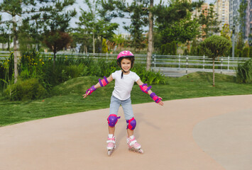 A little curly-haired girl rollerskates within the necessary facilities in the city. In a helmet...