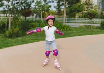 A little curly-haired girl rollerskates within the necessary facilities in the city. In a helmet...
