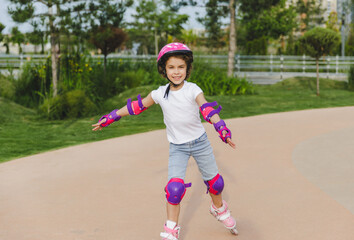 A little curly-haired girl rollerskates within the necessary facilities in the city. In a helmet and armbands