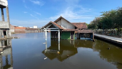 A house stands damaged after being submerged in floodwaters. Muddy walls, debris, and broken parts show the impact of the flood and the hardship faced by the residents.