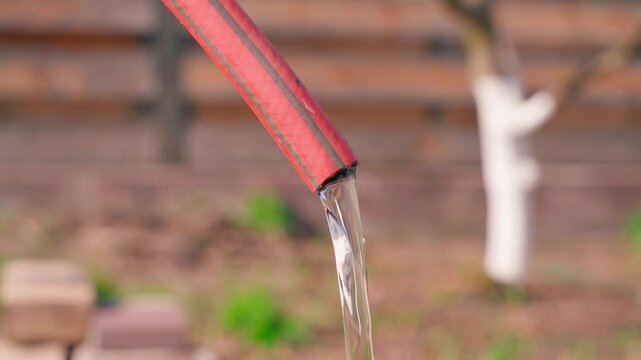 Water flows from a red hose in close-up in slow motion 