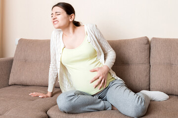 Pregnant woman with painful belly on sofa at home