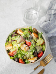 Salad with lettuce, tomatoes, croutons, olives and parmesan cheese in a bowl on a light background