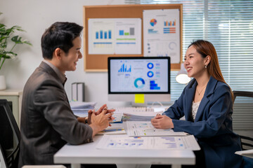 A man and a woman are sitting at a desk with a computer monitor in front of them