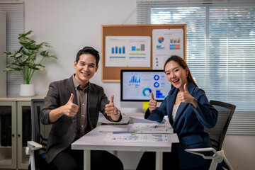 Two people are sitting at a desk with a computer monitor in front of them