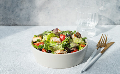 Salad with lettuce, tomatoes, croutons, olives and parmesan cheese in a bowl on a light background