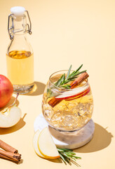 Apple cocktail or cider in a glass with ice, cinnamon and rosemary on a marble stand