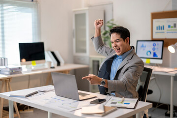A man in a suit is celebrating in front of a computer monitor