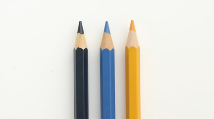 Three colored pencils: black, blue, and yellow with sharpened tips on a light background
