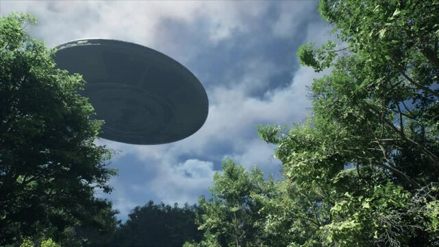 Breathtaking view up through the canopy in a forest as a huge circular UFO flying saucer spins slowly overhead casting its ominous shadow over the trees below