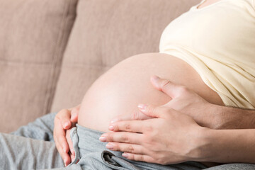 A young couple is expecting a baby. husband hugs the belly of his pregnant wife at home