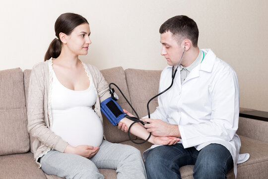 Young doctor is checking blood pressure of pregnant woman at home. High pressure problem during pregnancy concept - Powered by Adobe