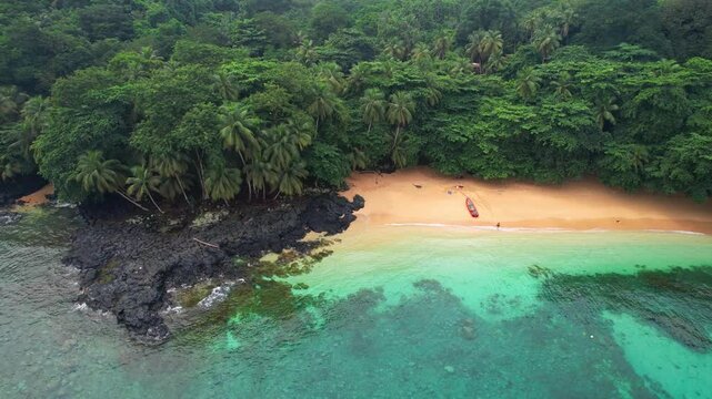 Flying backwards with a woman entering the water with a boat on the beautiful Margarida beach at Ilha do Principe (Prince Island) S&atilde;o Tom&eacute;,Africa