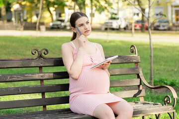 pregnant woman sits on a park bench and writes a to do list to the hospital