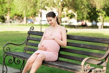 Pregnant young woman on bench sitting in the park. Pregnancy and motherhood. Healthy lifestyle