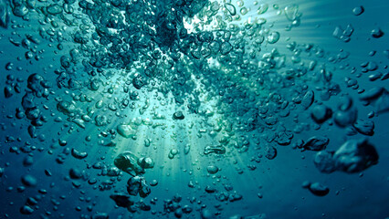 Underwater art photography. Air bubbles going towards the surface in sunlight in the deep blue sea.