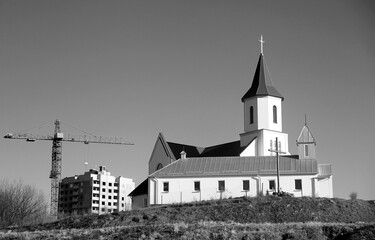 Old church with modern construction in background at daytime in urban setting.