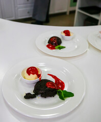 Delicious dessert served on white plates with chocolate cake, ice cream, and raspberry sauce at a kitchen