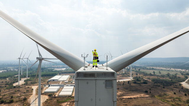 Electric engineer wearing Personal protective equipment working on top of wind turbine farm. - Powered by Adobe