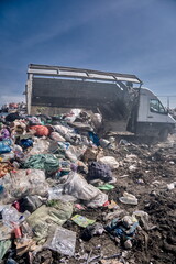 A truck unloads garbage at a landfill: piles of bags, plastic, and boxes form a heap of waste.	