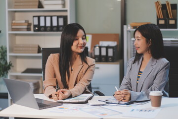 Two young Asian business woman talk, consult, discuss working with new startup project idea presentation analyze plan marketing and investment in the office.