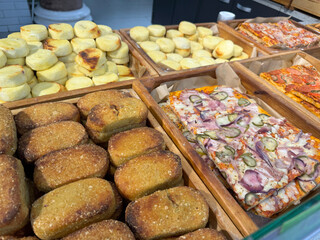 Various baked goods displayed at a store counter: bread rolls, mini cheesecakes, and pizza slices