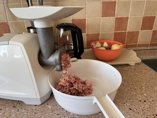 Meat grinder on a kitchen counter producing ground meat into a bowl. Prepping ingredients for...