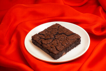 Chocolate brownie in the white plate on the red background  
